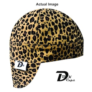 May include: A leopard print cap with a curved brim. The cap is tan with dark brown spots. A white tag with the letters "DK" is sewn on the front. The brand name "DK Caps" is printed in black.