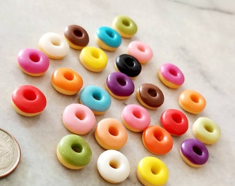 May include: A collection of 20 miniature donuts in various colors, including pink, yellow, green, blue, red, orange, white, brown, and purple. The donuts are arranged in a semi-circle on a white marble surface.