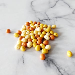 May include: A pile of small, round, ceramic beads in shades of yellow, orange, and white. The beads are smooth and have a slightly glossy finish.