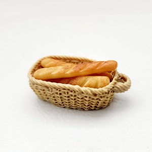 May include: A small wicker basket filled with several miniature loaves of bread. The basket is light brown and the bread is a light tan color.