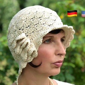 May include: A white crocheted cloche hat with a flower detail. The hat has a scalloped brim and is worn by a person with dark hair.