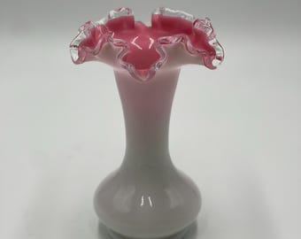 May include: A small, white and pink glass vase with a ruffled top. The vase has a silver trim around the top edge.