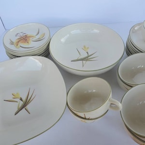 May include: A set of white ceramic dinnerware with a floral design featuring yellow and green accents. The set includes bowls, plates, and cups.