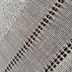 May include: Close-up of a white fabric with a woven pattern. The fabric has a delicate, open weave with a subtle texture.
