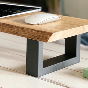 May include: A wooden monitor stand with a natural wood grain finish and dark gray metal legs. A laptop and a white computer mouse rest on the stand. The stand is designed to elevate a computer monitor.