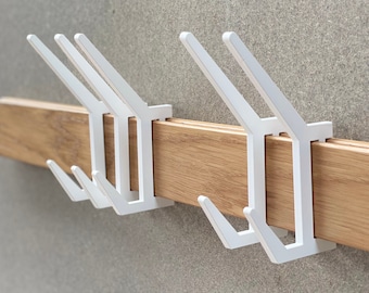 May include: White coat rack with five hooks mounted on a wooden wall. The hooks are made of metal and are shaped like a simple, modern design.
