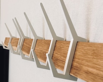 May include: A wooden wall-mounted coat rack with eight white metal hooks. The hooks are shaped like a V and are attached to a long, rectangular piece of wood.