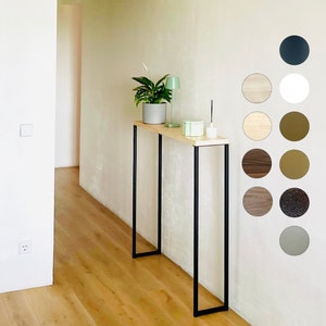 May include: A narrow console table with a black metal frame and a light wood top. The table is against a white wall with a variety of wood and paint colour swatches.