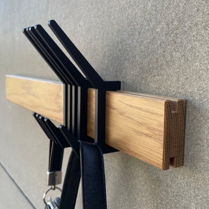 May include: A black metal coat rack with multiple hooks mounted to a wooden wall rail. A black leather handbag hangs from one of the hooks.