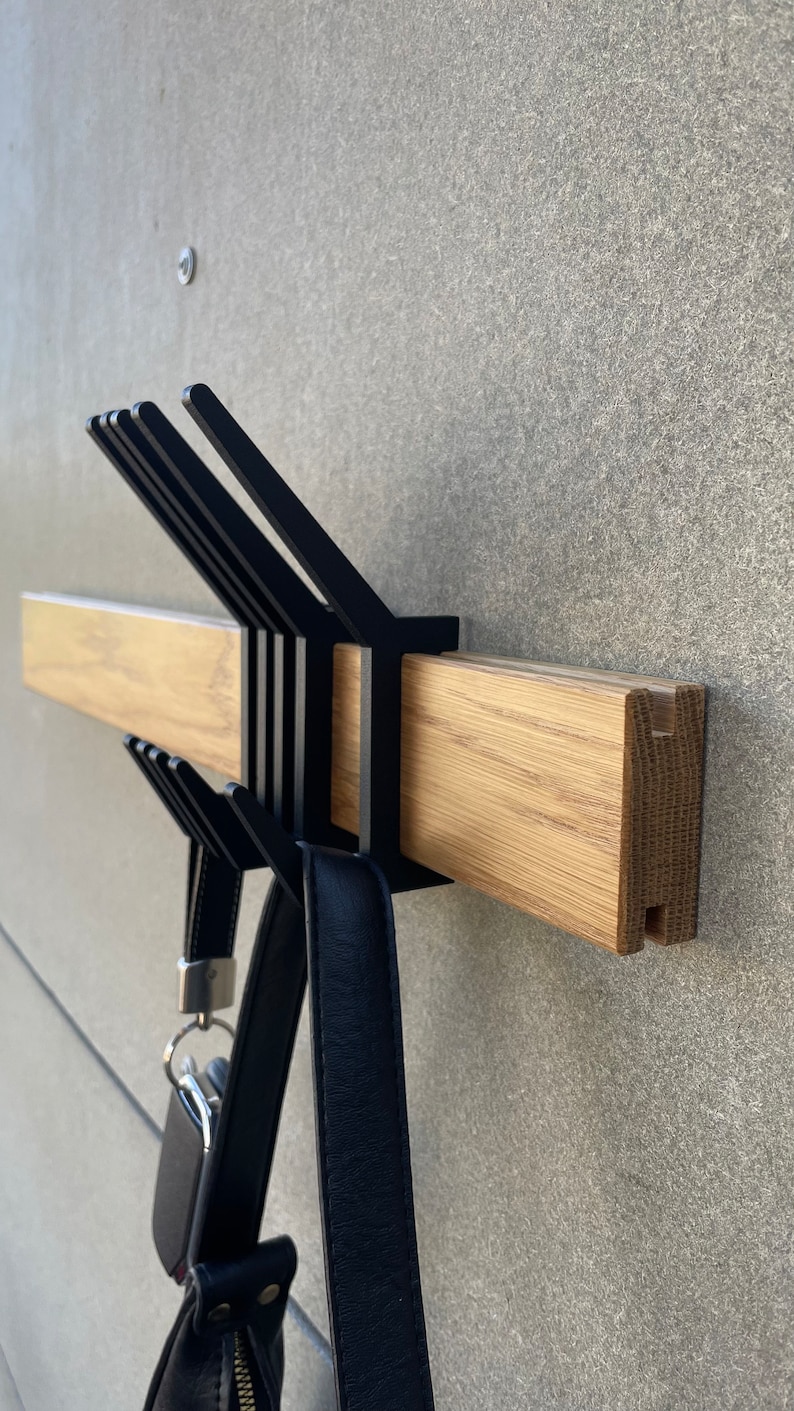 May include: A black metal coat rack with multiple hooks mounted to a wooden wall rail. A black leather handbag hangs from one of the hooks.