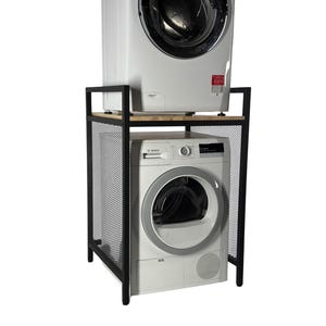 May include: A black metal laundry appliance stand with a wooden top, holding a white washing machine and a dryer. The stand has a mesh side panel. The appliances are stacked, with the dryer on the bottom.
