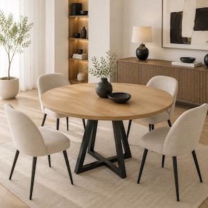 Op de afbeelding: Een ronde eettafel met een licht eikenhouten blad en een zwart metalen X-vormig onderstel, vergezeld door vier gestoffeerde stoelen met lichtbeige stoffen zittingen en zwarte metalen poten, geplaatst rond de tafel op een lichtgekleurd kleed.