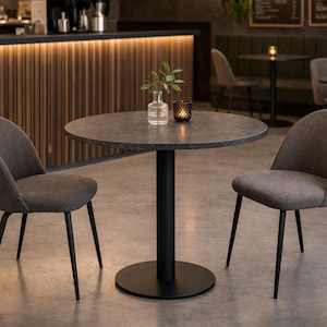 Può includere: Un tavolo rotondo grigio scuro con base a piedistallo nera, un piccolo vaso con vegetazione e un portacandele. Due sedie grigie imbottite con gambe nere circondano il tavolo. L'ambientazione è un moderno bar o ristorante.