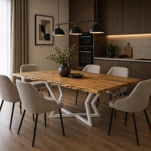 Peut inclure: Une salle à manger moderne avec une grande table en bois naturel et une base en métal blanc. Six chaises beiges rembourrées entourent la table. Un luminaire noir est suspendu au-dessus. Une œuvre d'art encadrée et un vase avec de la verdure sont également présents.