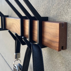 May include: A wooden wall-mounted coat rack with black metal hooks. The rack has a natural wood finish and is designed to hold coats, bags, and other items.