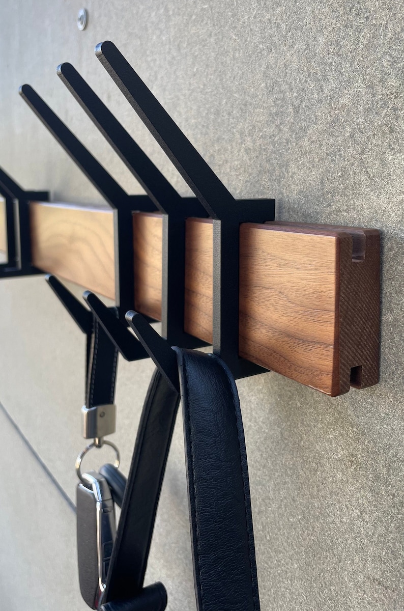 May include: A wooden wall-mounted coat rack with black metal hooks. The rack has a natural wood finish and is designed to hold coats, bags, and other items.