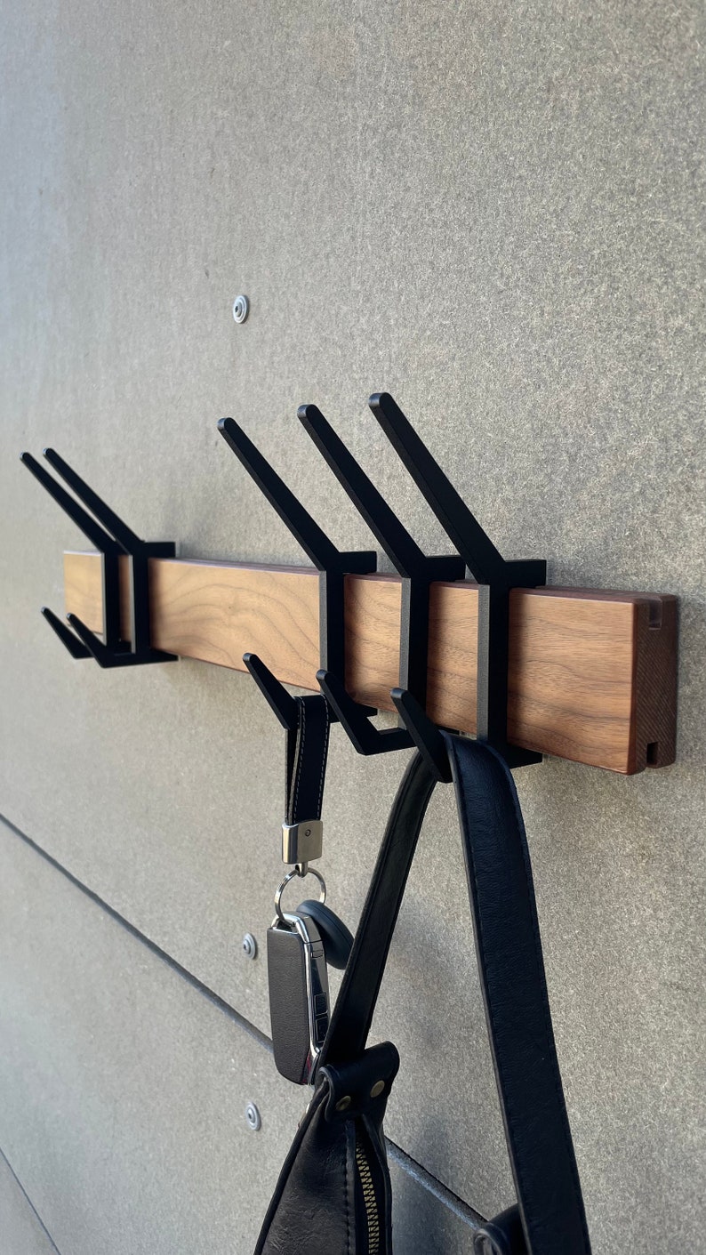 May include: A wooden wall-mounted coat rack with five black metal hooks. A black leather bag and a set of keys are hanging on the hooks.