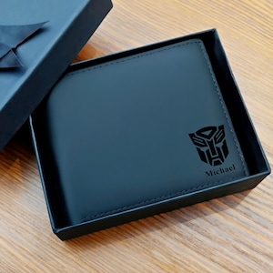 May include: Black leather wallet with a Transformers logo and the name "Michael" engraved on the front. The wallet is presented in a black gift box with a satin ribbon.