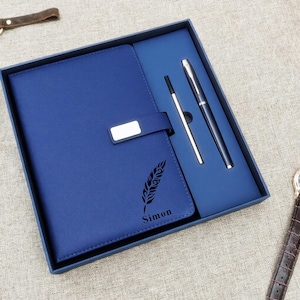 May include: A blue leather journal with a silver clasp, a black feather design, and the name "Simon" printed on the cover. The journal is packaged in a blue box with a pen and a stylus.