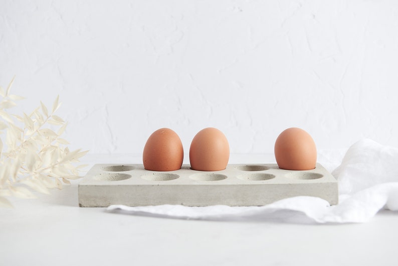 Puede incluir: Tres huevos marrones en un soporte para huevos de hormig&oacute;n gris con 12 ranuras individuales.
