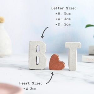 K&ouml;nnte beinhalten: Wei&szlig;e Betonbuchstaben "B" und "T" mit einem kleinen Kupferherz dazwischen. Die Buchstaben sind 5 cm hoch, 4 cm breit und 2 cm tief. Das Herz ist 3 cm breit.