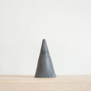 May include: A gray cone-shaped ring holder made of concrete.
