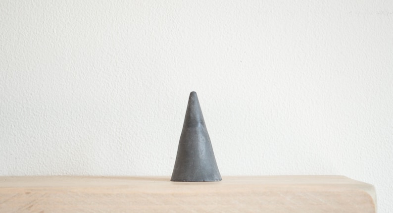 May include: A gray cone-shaped ring holder made of concrete.