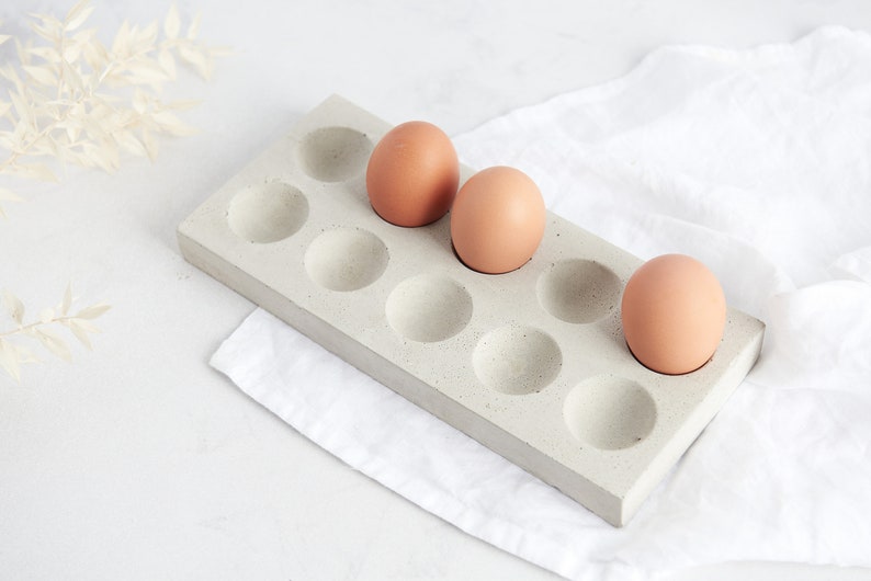 Puede incluir: Un soporte para huevos de hormig&oacute;n con 10 compartimentos individuales, tres de los cuales est&aacute;n llenos de huevos marrones.