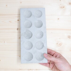 Puede incluir: Una bandeja de hormig&oacute;n gris con 12 hendiduras circulares. La bandeja est&aacute; dise&ntilde;ada para hacer peque&ntilde;as manualidades o servir aperitivos.