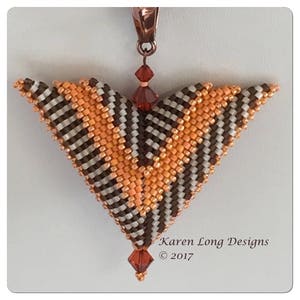 May include: A beaded pendant in a triangular shape, featuring a pattern of orange, brown, and white beads. The pendant has a copper-colored bail and is adorned with a dangling red crystal bead. The text "Karen Long Designs © 2017" is visible.