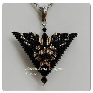 May include: A black, gold, and silver beaded pendant in the shape of a butterfly. The pendant is hanging from a silver chain. The pendant is a triangular shape with a pointed bottom. The text "Karen Long Designs © 2017" is visible below the pendant.