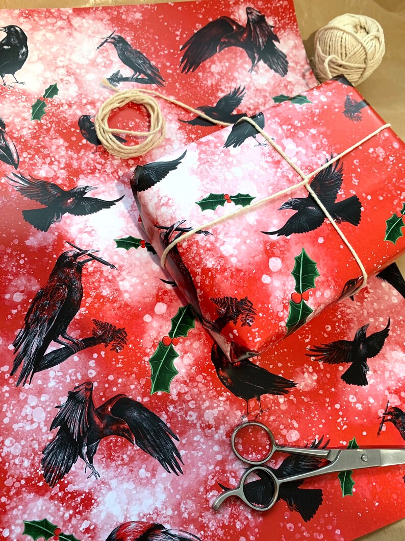 May include: Red wrapping paper with a pattern of black crows, holly, and white speckles. A wrapped gift is tied with twine. Scissors and a ball of twine are also visible.