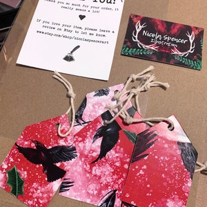 May include: A package with a thank you note, business card, and decorative tags. The tags feature a red background with black raven illustrations and are tied with twine. The thank you note includes the text "Thank You!" and the Etsy shop URL.