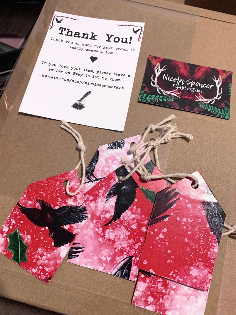 May include: A package with a thank you note, business card, and decorative tags. The tags feature a red background with black raven illustrations and are tied with twine. The thank you note includes the text "Thank You!" and the Etsy shop URL.