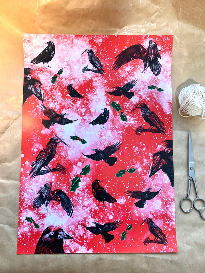 May include: Red wrapping paper with a pattern of black crows in various poses, with sprigs of holly and white accents. A ball of white twine and silver scissors are next to the paper.