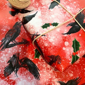 May include: Red wrapping paper with black raven illustrations and white speckles. A wrapped gift is tied with twine and decorated with holly. A ball of twine and scissors are also visible.