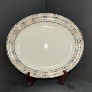 May include: A large, oval-shaped serving platter with a cream-colored background and a decorative border. The border features a repeating pattern of black and gray stylized knots and swirls on a light peach background.