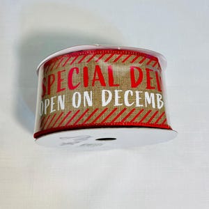 May include: A roll of decorative ribbon with the words "SPECIAL DEL" and "OPEN ON DECEMB" in red and white. The ribbon has a burlap texture with red diagonal stripes.