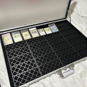 May include: Open silver display case with a black grid interior, holding several graded trading cards. The case is open, revealing the cards in protective holders. The case has a silver handle and hinges.