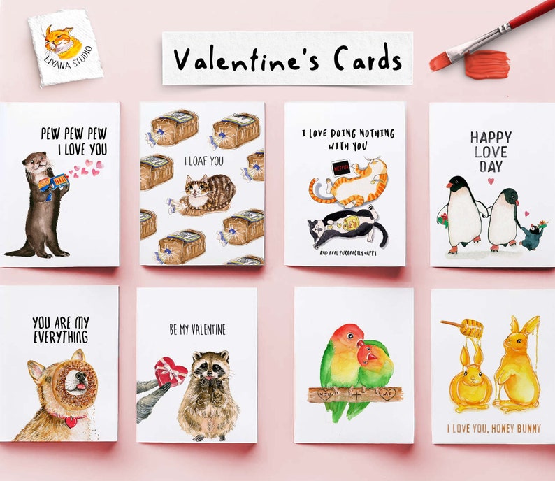 May include: A set of eight Valentine's Day cards featuring various illustrations and messages. The cards are printed on white cardstock and have a watercolor style. The illustrations include a penguin couple, a cat loafing, a raccoon with a heart, a pair of lovebirds, and a honey bunny.