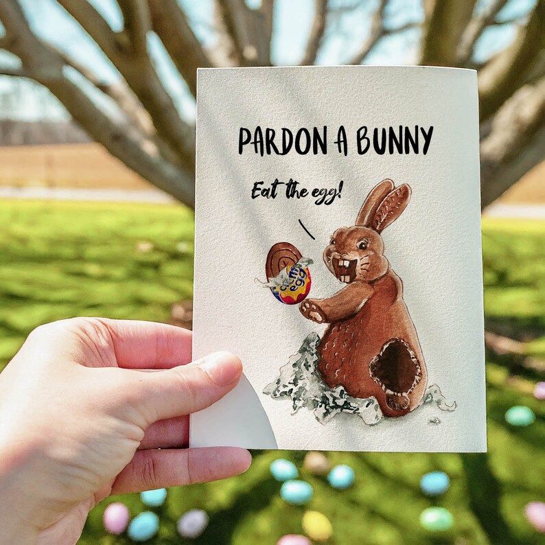 May include: A white card with the text "Pardon a bunny, Eat the egg!" and a watercolor illustration of a brown bunny holding a chocolate egg.