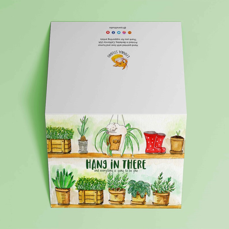 Peut inclure: Une illustration aquarelle d'une plante suspendue avec un chat dormant dans le pot. Le texte "HANG IN THERE and everything is going to be fine" est &eacute;crit sous la plante. L'illustration est sur une carte avec un fond vert.
