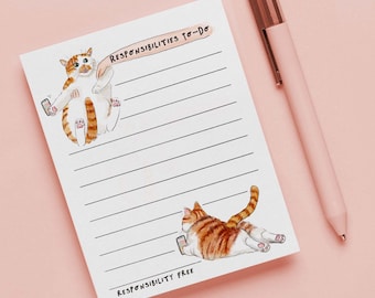 May include: A white notepad with horizontal lines and cat illustrations. The notepad has the text "RESPONSIBILITIES TO-DO" and "RESPONSIBILITY FREE". A pink pen with a rose gold clip rests on a pink surface.