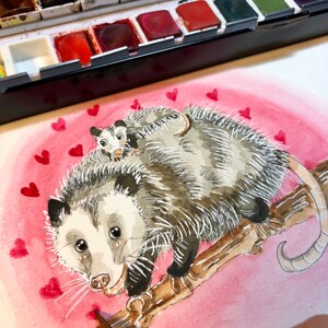 May include: Watercolor painting of two opossums on a branch with a pink background and red hearts. The opossums are facing the viewer and the larger opossum is holding the smaller opossum on its back.