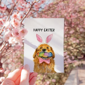 May include: A watercolor illustration of a golden retriever dog wearing bunny ears and holding a basket of Easter eggs in its mouth. The card says "Happy Easter".