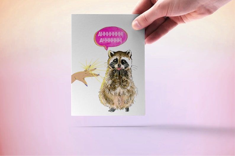 May include: A greeting card with a cartoon raccoon with a pink speech bubble that says "AHHHHHHH! AHHHHHHH!" The raccoon is looking up at a hand with a ring on it.