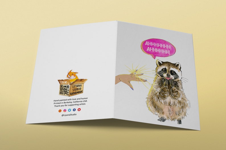 May include: A greeting card with a raccoon illustration and the text "AHHHHHHH! AHHHHHH!" in a pink speech bubble. The raccoon is looking up with a surprised expression and has its paws together. The card is white with a light yellow background.