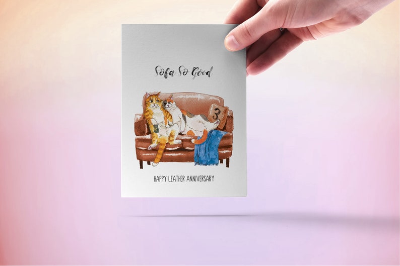 May include: A greeting card with a watercolor illustration of two cats sitting on a brown leather sofa. The text on the card reads "Sofa So Good" and "Happy Leather Anniversary".