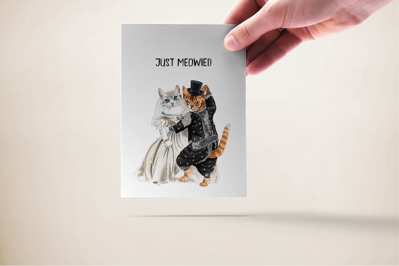 May include: A wedding card with a white cat wearing a veil and a brown cat wearing a tuxedo and top hat. The text on the card reads "Just Meowied".