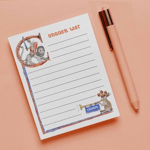 May include: A white notepad with the words "ORDER LIST" in red, featuring illustrations of a rabbit and lion. A pink pen rests beside the notepad on a pink surface. The notepad has lined pages for writing.